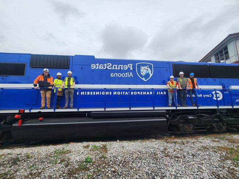 Rail Transportation Engineering students and faculty pose with a Penn State-branded locomotive